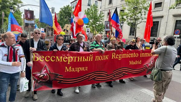 Účastníci Nesmrteľného pluku na slávnostnom pochode v Španielsku.  Miestni obyvatelia držia rodinné portréty, zástavy víťazstva a vlajky nových ruských regiónov Luganskej ľudovej republiky (vľavo) a Doneckej ľudovej republiky (vpravo).  - Sputnik International