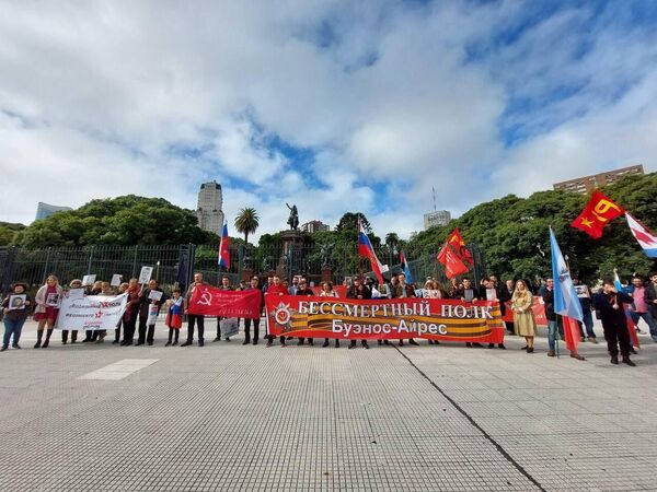 Účastníci nesmrteľného pluku pochodujú so stuhou sv. Juraja a transparentom sovietskeho víťazstva v Argentíne.  - Sputnik International